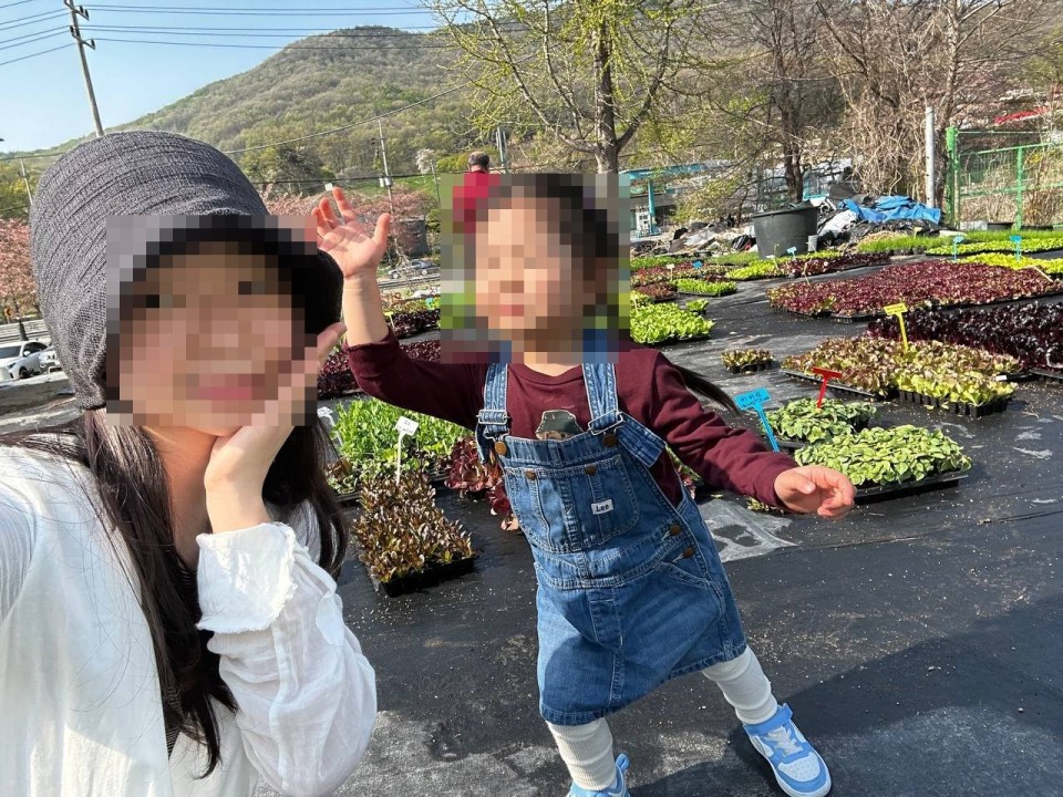 엄마와 아이가 한밭농원에서 다양한 색깔의 잎채소 모종들을 배경으로 함께 셀카를 찍는 모습